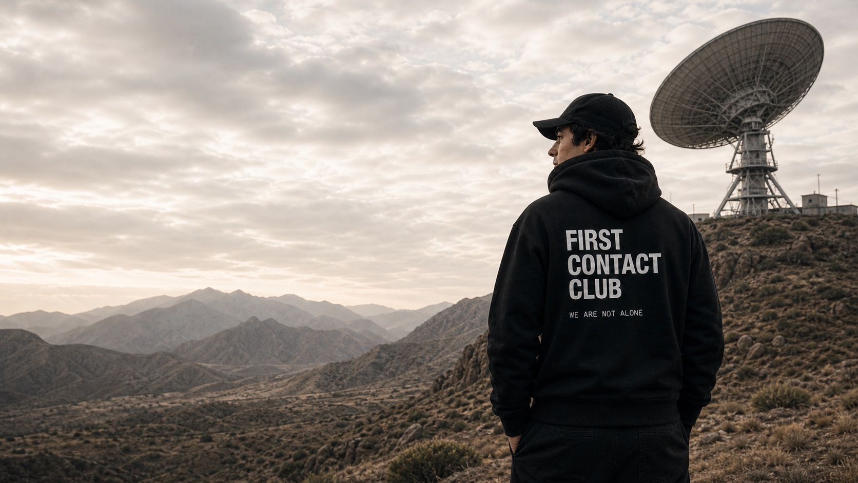 Model wearing a First Contact Club hoodie at a mountain radar station